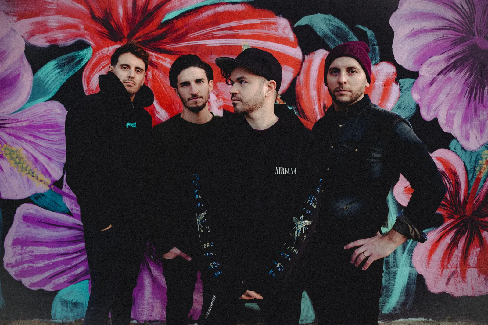 The four members of Melody Fall dressed in black in front of a mural of giant pink and purple flowers